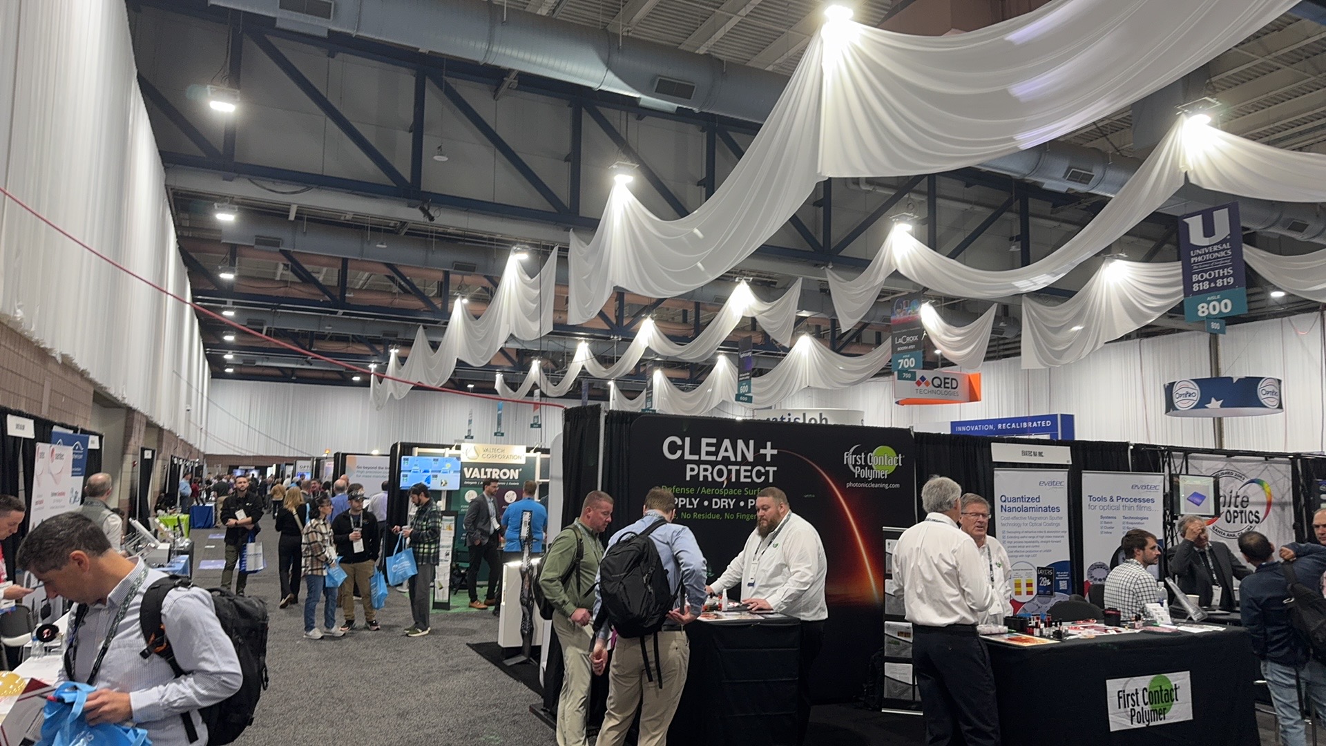SPIE Optifab 2025 main aisle in Rochester with Valtron, First Contact Polymer, Evatec, and White Optics booths